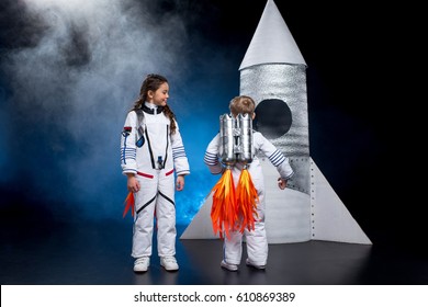 Little boy and girl in astronaut costumes standing near rocket 