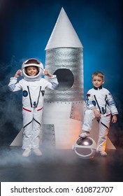 Little boy and girl in astronaut costumes standing near rocket and looking at camera
