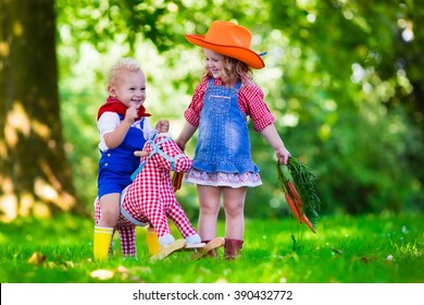 Little Boy And Girl Dressed Up As Cowboy And Cowgirl Playing With Toy Rocking Horse In Park. Kids Play Outdoors. Children In Halloween Costumes At Trick Or Treat. Toys For Preschooler Or Toddler Child