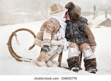 Little Boy And Girl Kissing While Sitting On A Sled In Winter