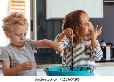 Little Boy And Girl Mixing Batter In A Bowl For Baking, With Girl Licking Her Fingers. Small Kids Baking In The Kitchen.