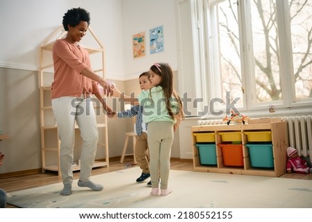 Little boy and girl playing ring-around-the-rosy with their African American teacher at kindergarten. 