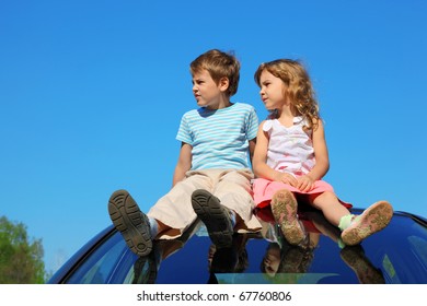 Little Boy And Girl Sitting On Car Roof On Blue Sky, Looking To Left Side