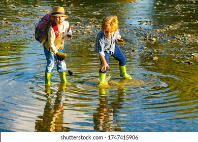 Little Boy And Girl Throws Stones Into The Water On The Shore Of A Lake. Children Throw Stones At The Water. Beautiful Children Throws A Rock At The River. Skipping Rocks