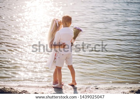 Little boy and girl in a white dress with a hat with a beautiful bouquet of flowers walking along a sandy beach