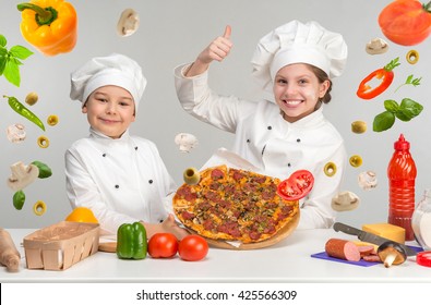 Little Boy And Girl In White Uniform Of Chef By The Table With Flying Pizza