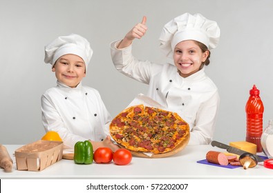 Little Boy And Girl In White Uniform Of Chef By The Table With Pizza