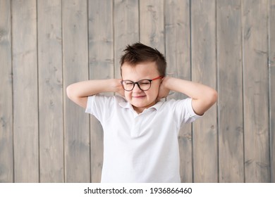 Little Boy In Glasses Suffering From Ear Pain. Kid Raises Two Hands To Cover His Ears. The Boy Is Not Happy And Has Earache