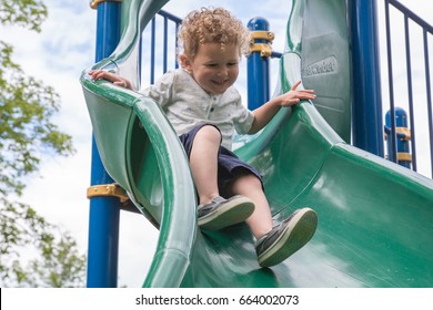 Little Boy Is Going Down A Slide At The Playground. He Is Laughing And Having Fun On The Jungle Gym At The Park. He Is In Preschool. Back To School, Recess, Summer Vacation 