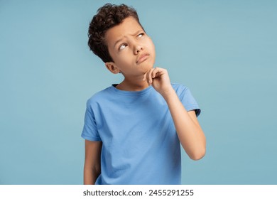 Little boy with hand on chin thinking about question, pensive expression, posing in studio, isolated on blue background. Advertisement concept - Powered by Shutterstock