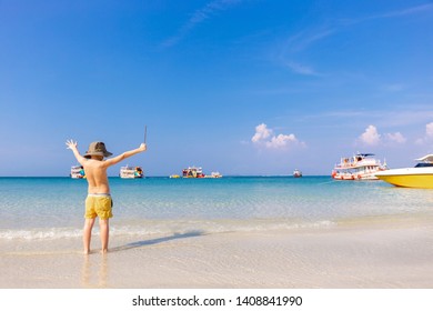 Little Boy In Hat Walking On A Tropical Beach. Cute Boy Having Fun On The Beach Vacation. He Spread His Arms Like A Conductor. Alone On The Beach.