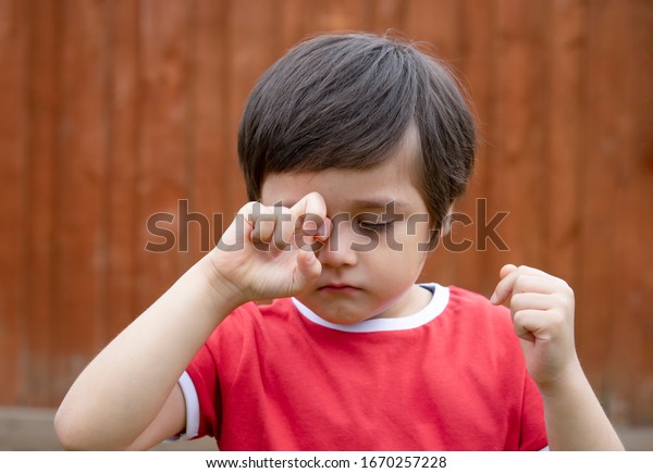 Little boy is having\
allergy rubbing his eye, Kid scratching his eyes while playing\
outdoor in summer, Child having allergy itchy face and sneezing\
while playing outdoor.