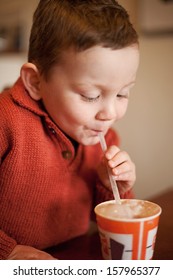 Little Boy Having Fun Blowing Bubbles Through A Straw Into His Chocolate Millksake