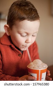 Little Boy Having Fun Blowing Bubbles Through A Straw Into His Chocolate Millksake