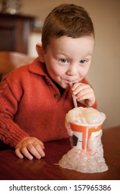 Little Boy Having Fun Blowing Bubbles Through A Straw Into His Chocolate Millksake