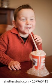 Little Boy Having Fun Blowing Bubbles Through A Straw Into His Chocolate Millksake