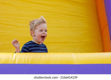 Little boy having fun in inflatable castle playground. Furious child shouts loudly. Bright yellow rubber trampoline background, there is free copy space. - Shutterstock ID 2166414139