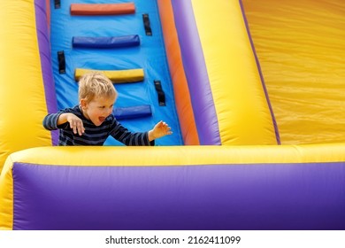 Little boy having fun on inflatable obstacle course. Joyful child naughty, intense raging on colorful inflatable trampoline with ladder. Children's leisure.