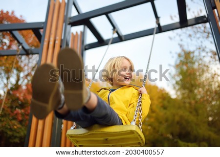 Little boy having fun on a swing on the playground in public park on autumn day. Happy child enjoy swinging. Active outdoors leisure for child in city