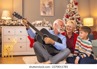 Little boy having fun spending winter holidays with grandparents, grandfather playing the guitar while his wife and grandson singing on Christmas day at home - Powered by Shutterstock