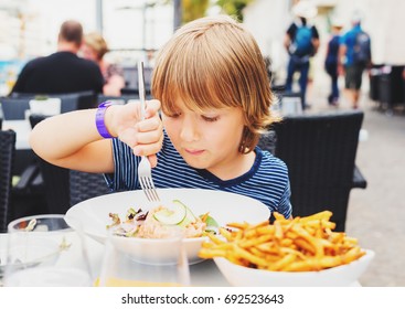 Little Boy Having Lunch In The Restaurant, Child Eating Fresh Salmon Salad And French Fries 