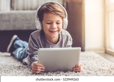 Little boy in headphones is using a digital tablet and smiling while lying on the floor at home - Powered by Shutterstock