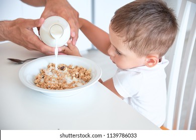 Little Boy Helps Dad Pour Milk Into Oatmeal. Quick Breakfast At Home