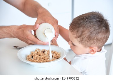 Little Boy Helps Dad Pour Milk Into Oatmeal. Quick Breakfast At Home