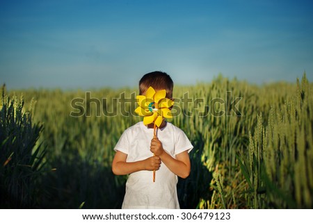 Little boy hides behind yellow pinwheel on blue sky and green field background