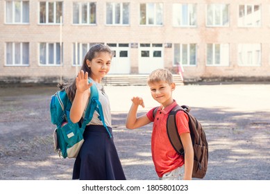 Little Boy And His Elder Sister Waving Goodbye To Parents On Their Way To School, Standing In Front Of Building Of Conventional School