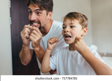 Little boy with his father in bathroom cleaning teeth with dental floss. Both looking in mirror and brushing teeth.