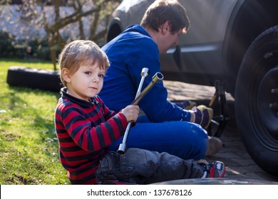 Little boy and his father changing wheel on car with pneumatic wrench