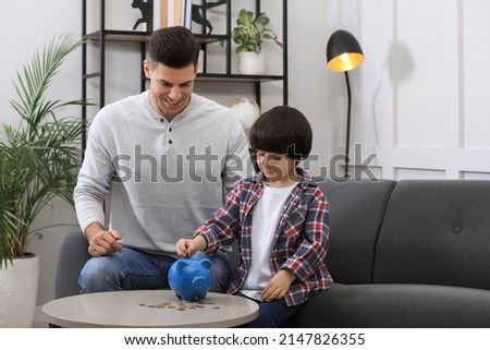 Little boy with his father putting coin into piggy bank at home