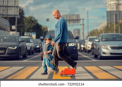Little boy with his father and a red toy track are crossing the street on crosswalk. A lot of cars are waiting them. Image with selective focus and toning