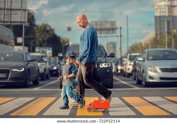 Little boy with his father and a red toy\
track are crossing the street on crosswalk. A lot of cars are\
waiting them. Image with selective focus and\
toning