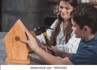 Little Boy And His Mother Building A Wooden Birdhouse With Hammer