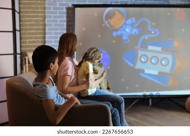 Little boy with his mother and sister watching cartoons on projector screen at home