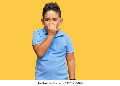 Little Boy Hispanic Kid Wearing Casual Clothes Smelling Something Stinky And Disgusting, Intolerable Smell, Holding Breath With Fingers On Nose. Bad Smell 