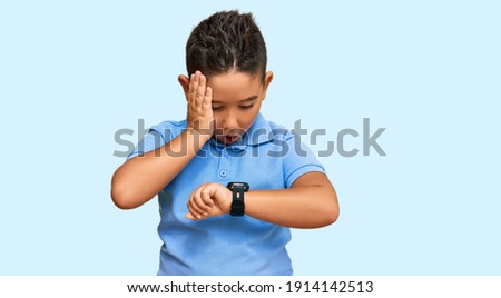Little boy hispanic kid wearing casual clothes looking at the watch time worried, afraid of getting late 