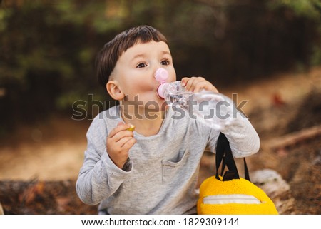 Little boy hold bit of apple or pear fruit, child relaxing, resting after hiking on mountains trail, kid drink water, backpack taking a snack in a forest trip, children in camping in vacation. 