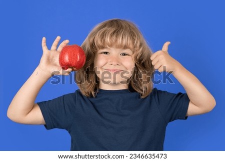Little boy holding apple with fynny face. Kid eats healthy food.