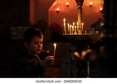 Little boy holding candle on dark background. A Child lights a candle in a chapel
