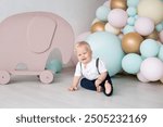 Little boy at home dressed in a suit with trousers on pull-ups and a shirt against the background of colorful balloons and a toy elephant. Family and childhood concept, holiday