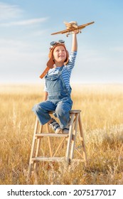 Little boy imagines flying. Cheerful and happy child plays with a model airplane and dreams of becoming a pilot in the field against the blue sky. - Shutterstock ID 2075177017