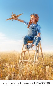 Little boy imagines flying. Cheerful and happy child plays with a model airplane and dreams of becoming a pilot in the field against the blue sky. - Shutterstock ID 2111604029