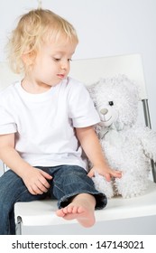 The little boy in jeans with a toy bear sits on a chair