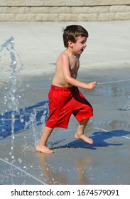 Little Boy Joyously Dashes About A Water Park In Arkansas.  He Has On A Huge Grin And Is Wearing A Pair Of Red Swim Trunks.