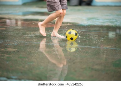 Little boy kicking ball in the water logging on the street