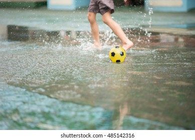 Little boy kicking ball in the water logging on the street