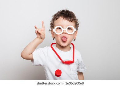 little boy, kid plays a doctor. Closeup portrait of a child in a white doctors glasses with a red stethoscope on his neck shows Horns hand, pulled out and shows tongue. that rocks 
